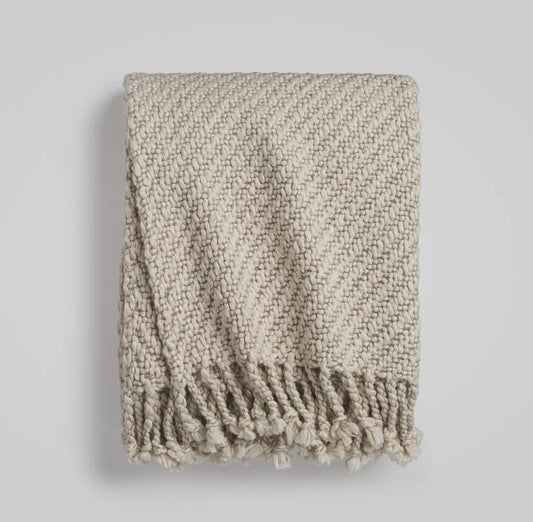 Textured beige throw blanket with fringes on a light gray background