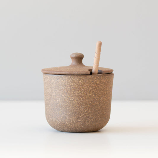 Handmade ceramic honey jar with wooden dipper on rustic wooden tray