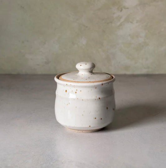 White ceramic jar with a lid on a gray surface with a neutral background