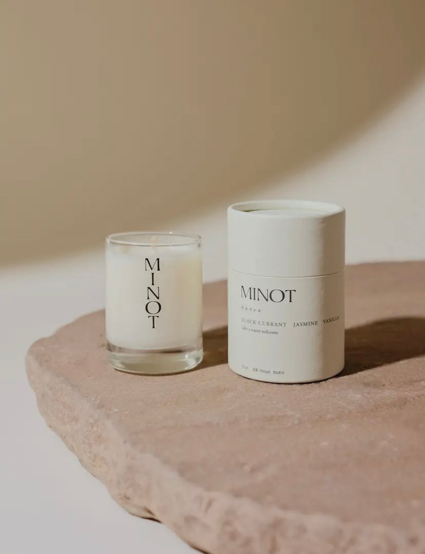 Candle and its packaging labeled 'MINOT' on a stone surface with a neutral background
