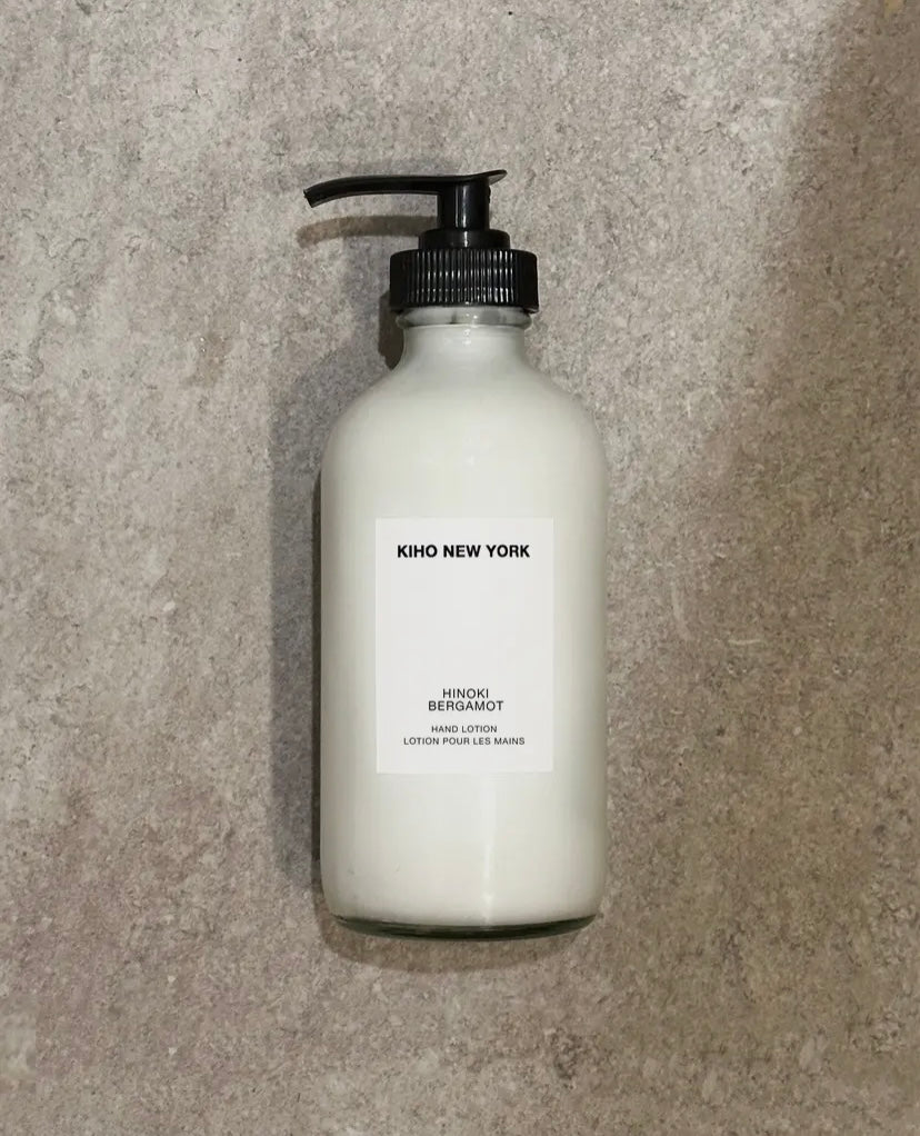 White bottle of Hinoki Bergamot soap with black pump on a gray concrete background.
