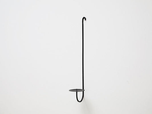 A minimalist black iron candle holder with a single arm, mounted on a wall, with a small platform for holding a candle.