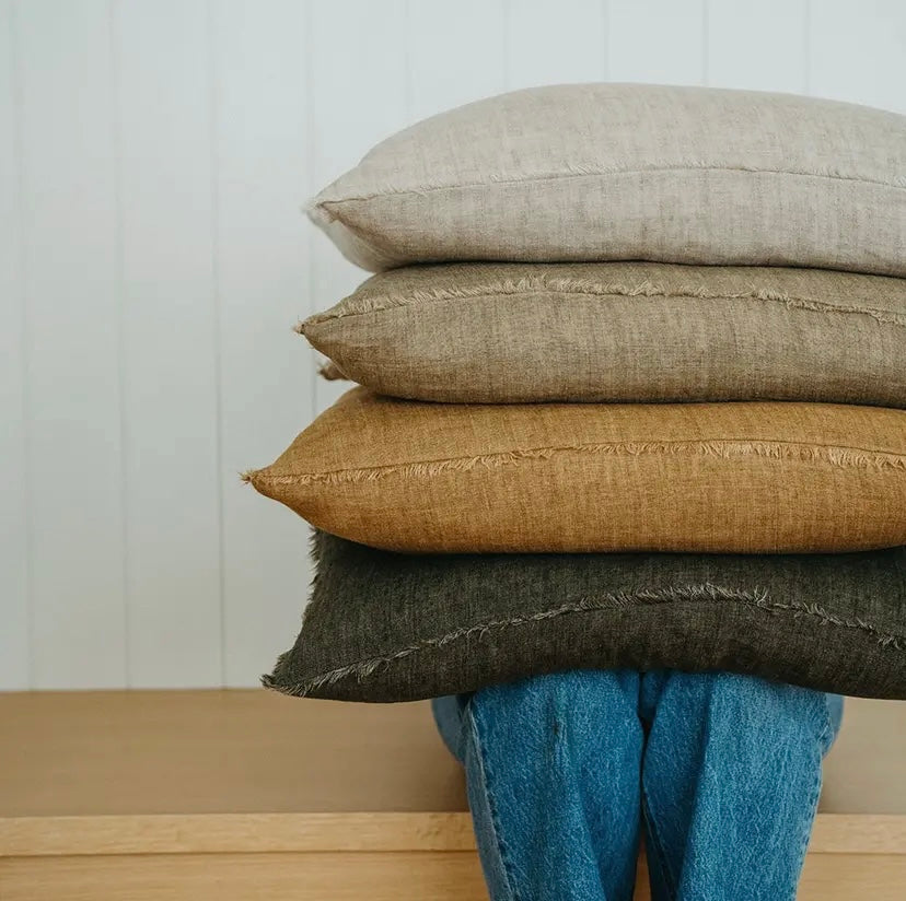 Stack of textured pillows in various colors on a wooden surface with a light background