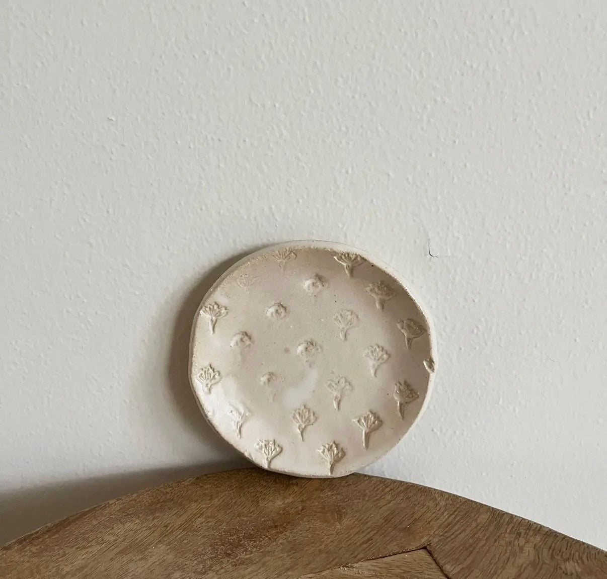 Round ceramic dish with floral patterns on a wooden surface and light gray wall background
