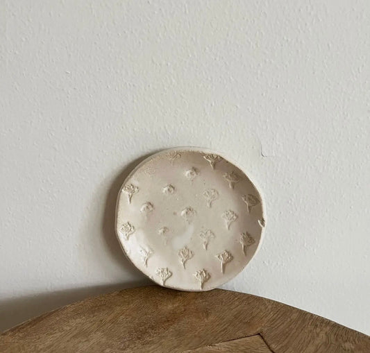 Round ceramic dish with floral patterns on a wooden surface and light gray wall background
