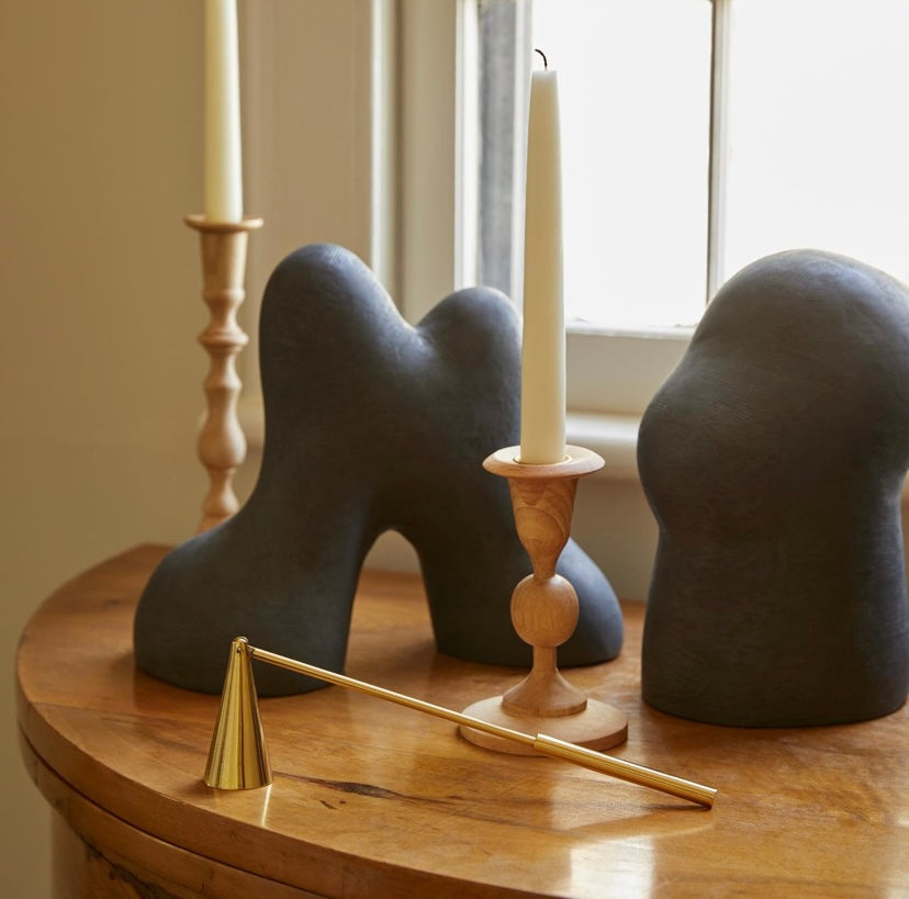 Decorative candle holders with featured candle snuffer in foreground on a wooden surface with a window in the background