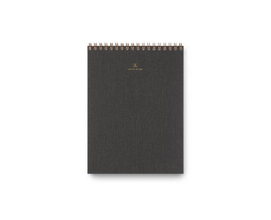 A charcoal, top-bound notepad with a waterproof cotton bookcloth cover and brass wire-o binding.