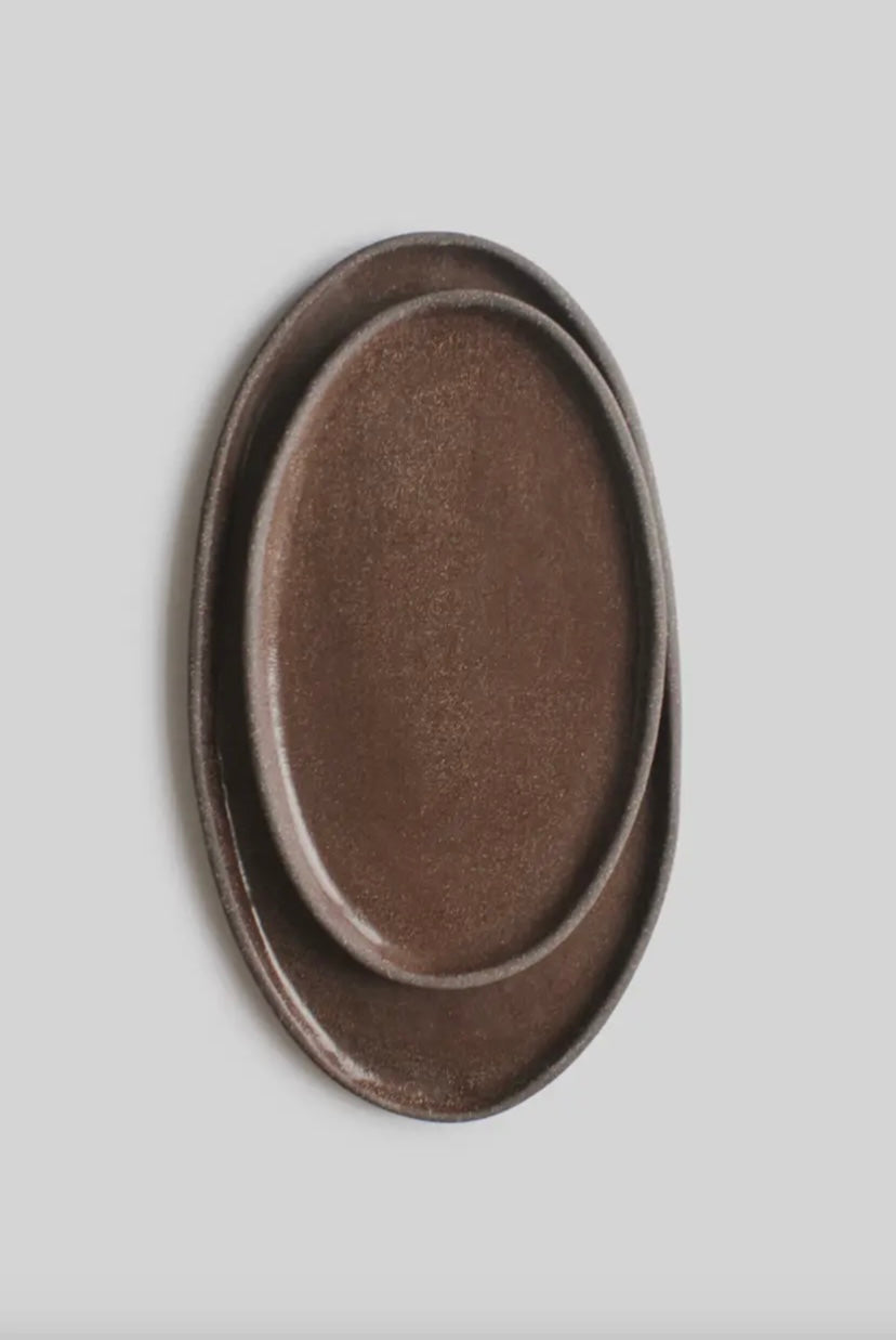 Brown ceramic oval platter on a light gray background turned vertically.