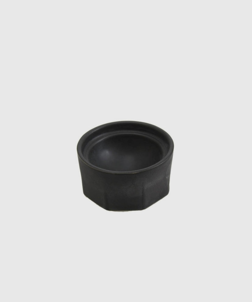 Close-up of black porcelain salt cellar showing faceted texture and spherical interior.

