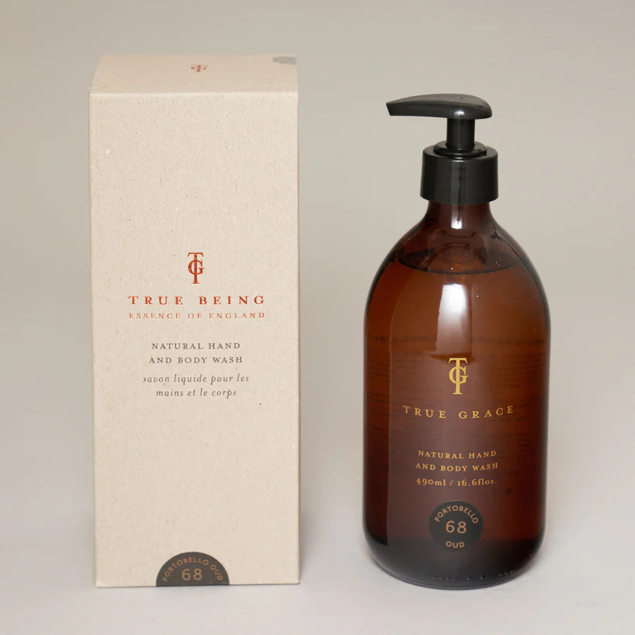 A pump bottle of True Grace hand and body wash with a beige label and black liquid, displayed next to its packaging box.