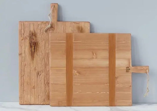 Two Pine Charcuterie Boards, showing front and back sides, leaning against a wall. The large board has two vertical strips of contrasting timber, and the medium board shows the natural grain of the wood.
