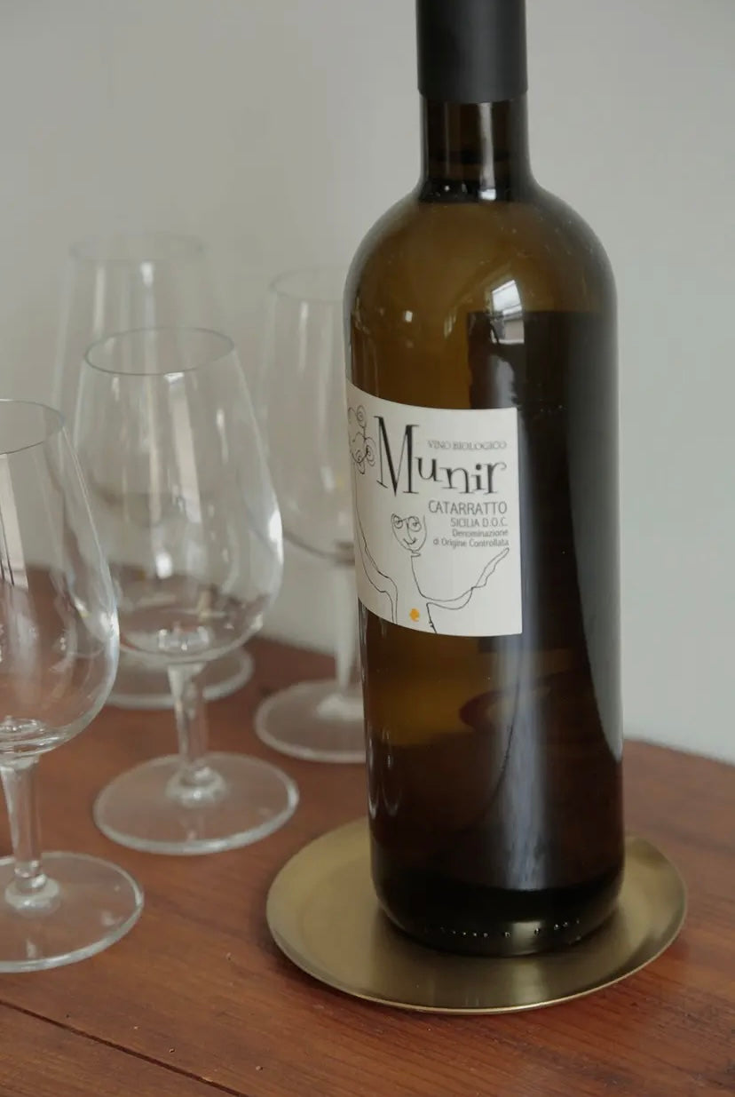 Wine bottle on a brass plate sitting on a wooden table with wine glasses in the background