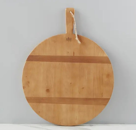 A round pine charcuterie board from Etu Home with two strips of contrasting timber on one side, hanging on a wall hook.