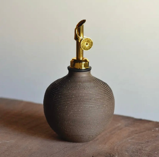 Brown ceramic oil dispenser with gold nozzle on a wooden surface