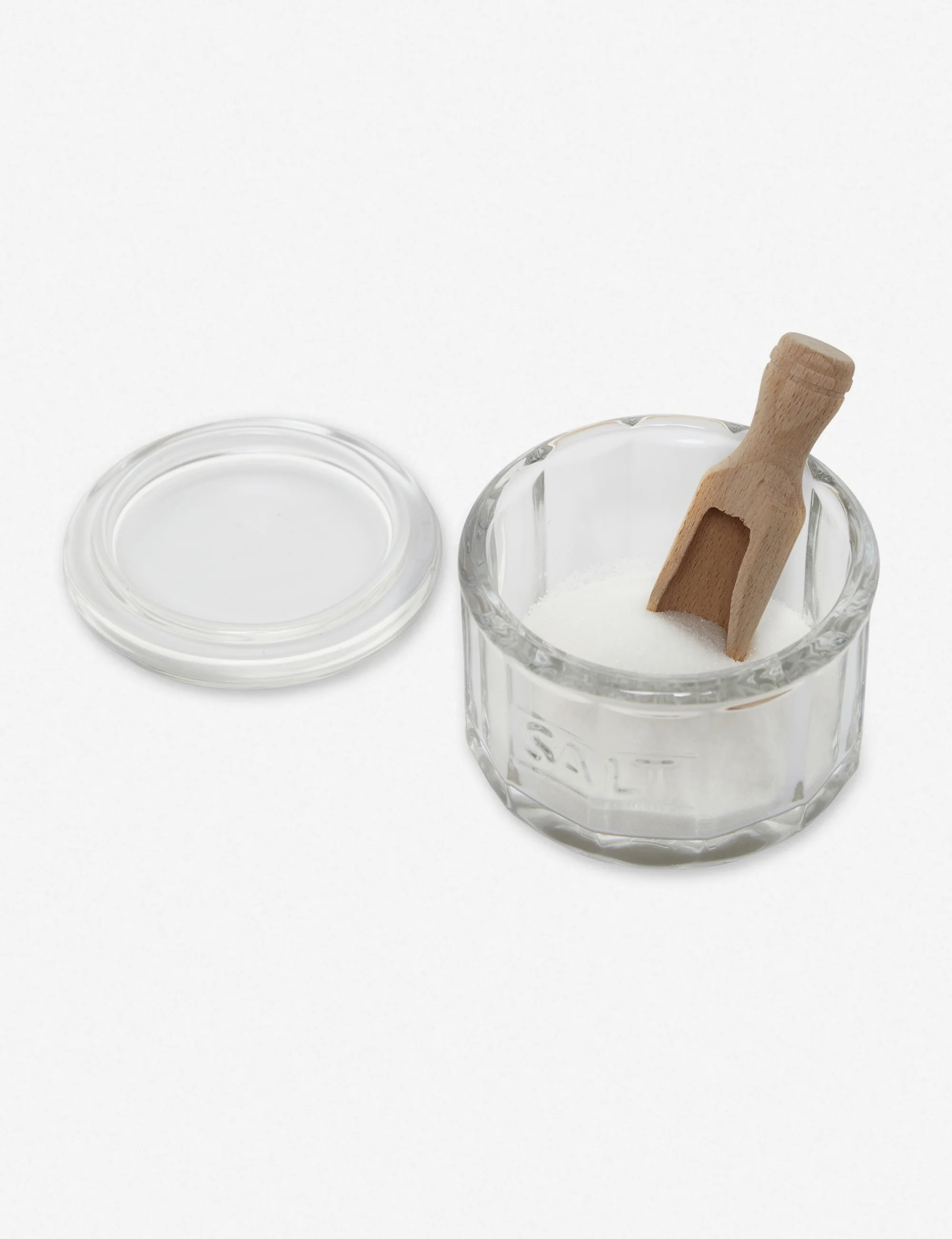 Vintage-style glass salt pot with wooden scoop on kitchen counter.
