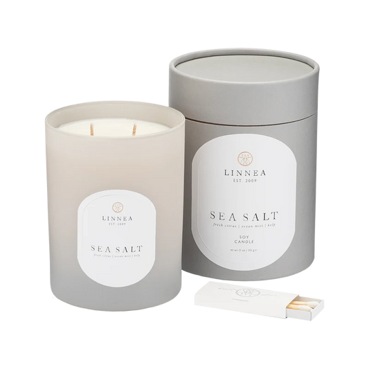 A LINNEA soy candle handcrafted with a Sea Salt fragrance, displayed in a gray cylindrical container with a lid, including a double cotton wick and a matchbox.