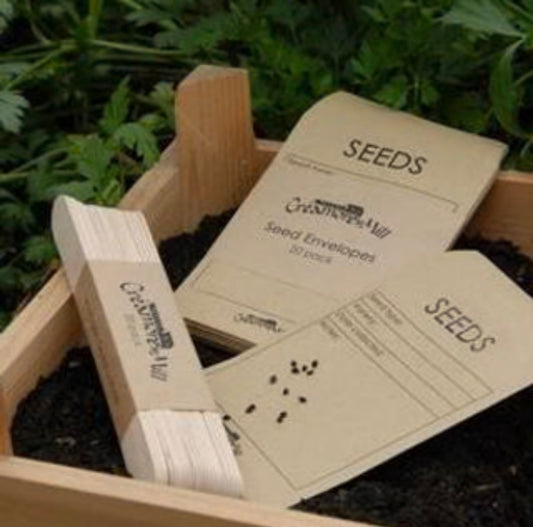 A stack of beige seed envelopes, placed in a wooden garden bed.