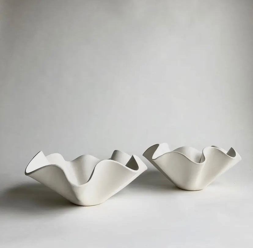 Two white ceramic ruffle bowls of different sizes placed on a neutral surface.