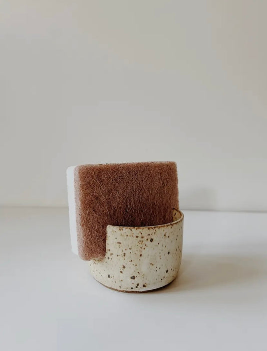 Speckled ceramic sponge holder with a brown sponge.
