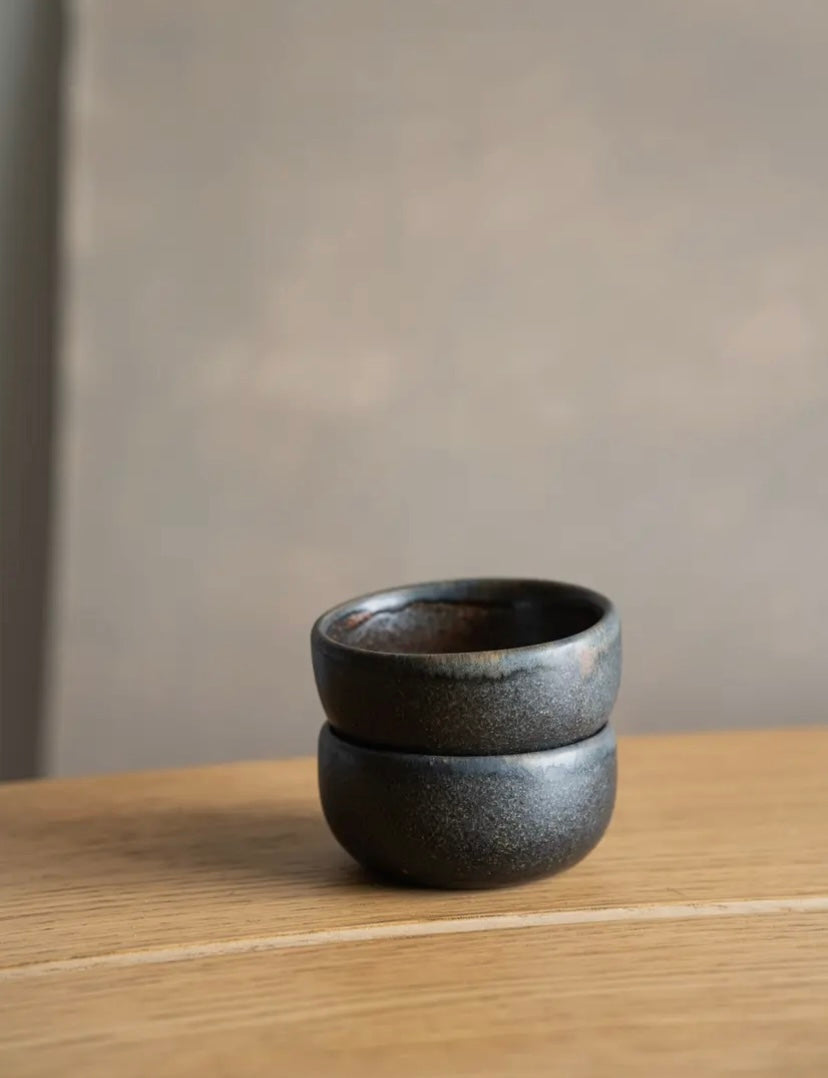 Two black ceramic cups stacked on a wooden surface with a neutral background.