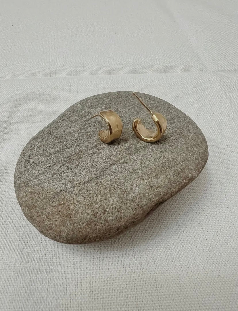 Pair of gold hoop earrings on a gray stone with a light gray background