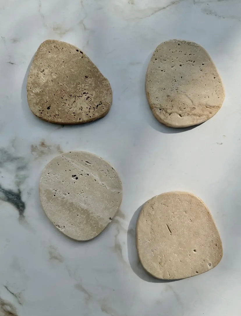 Four beige stone coasters on a marble surface