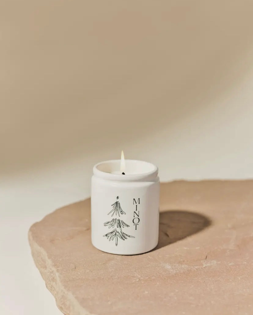 White candle in a container with 'Mint' text on a beige surface by MINOT