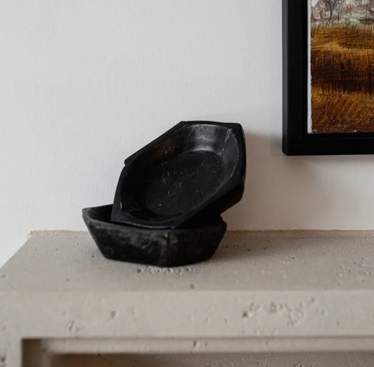 Two black marble bowls stacked on a concrete mantle with a framed picture in the background.
