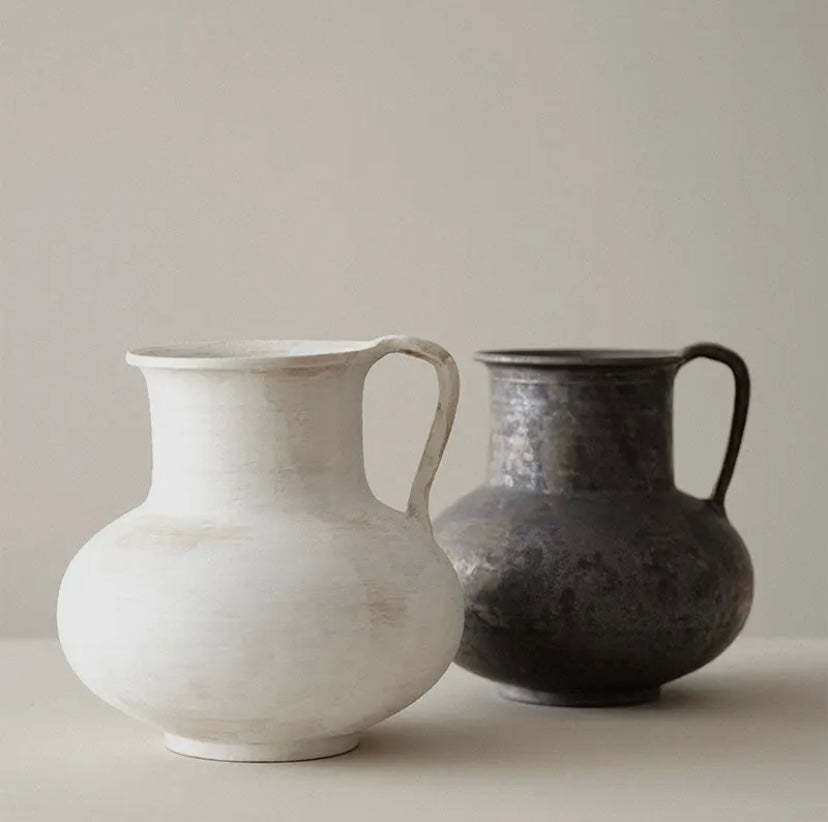 Two wabi sabi ceramic jugs, one white and one black, on a neutral background