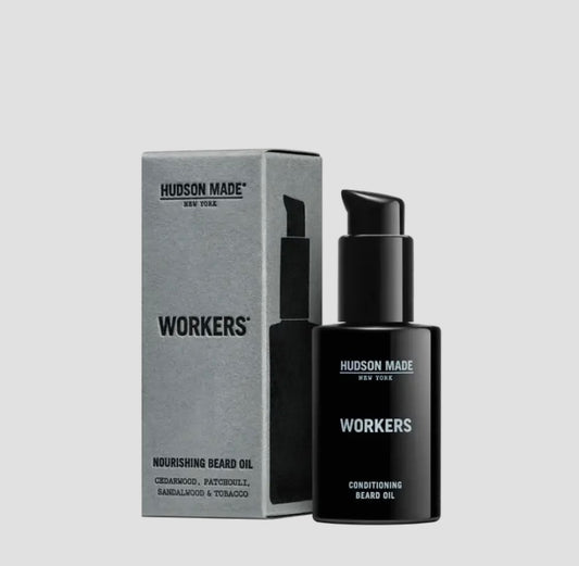 A black bottle of Hudson Made Workers Beard Oil with a pump, in front of its gray box packaging labeled 'nourishing beard oil'.