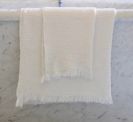 A white waffle weave bath towel hanging on a marble surface, showcasing its texture and size.